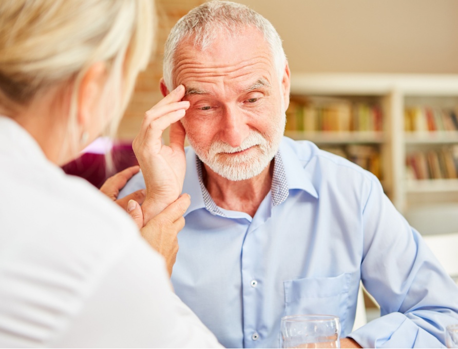 An older man touching his head in confusion while a doctor comforts him.