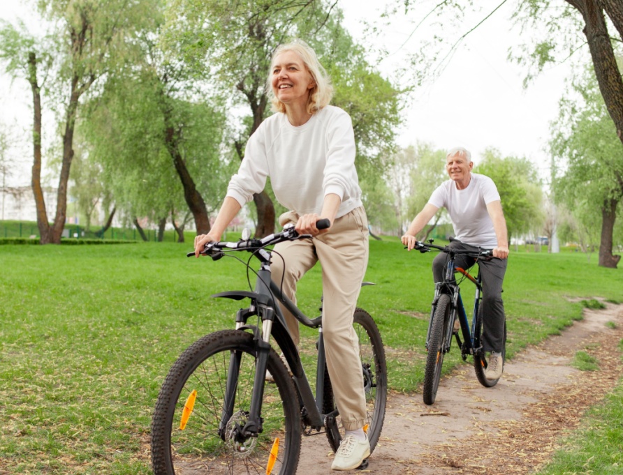 An elderly couple riding their bikes in the park.