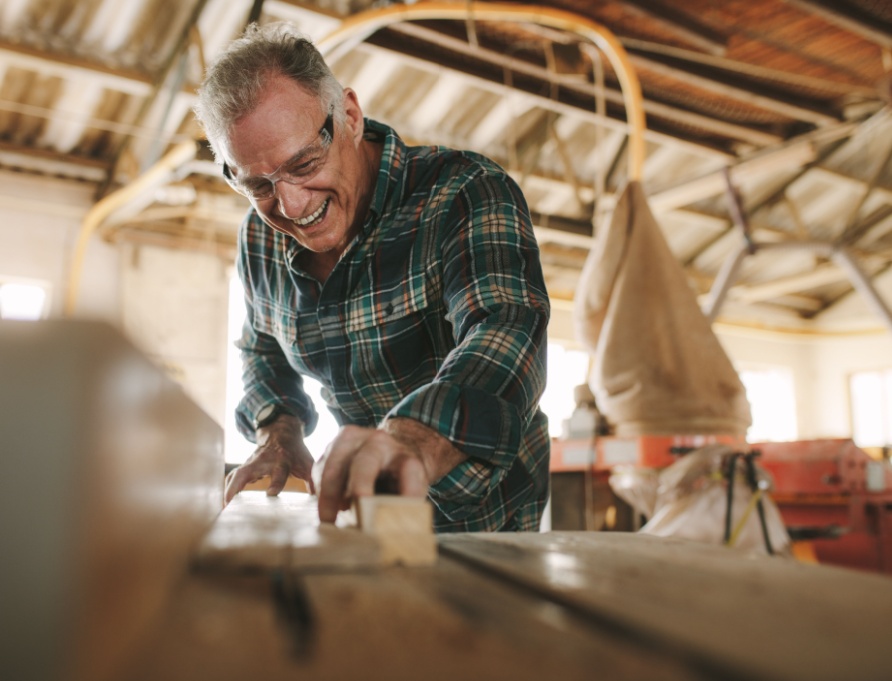 A senior man cutting wooden planks in a workshop.