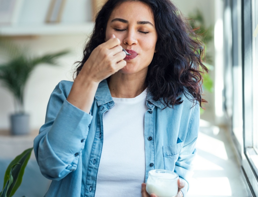 A woman eating a pot of yoghurt.