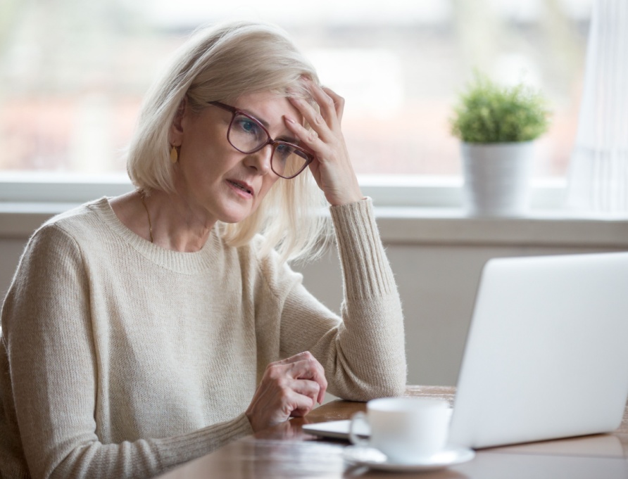 A retired woman looking worried while using a laptop.