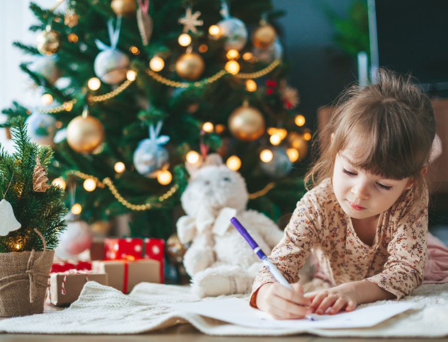 A girl writing a letter in front of a Christmas tree.